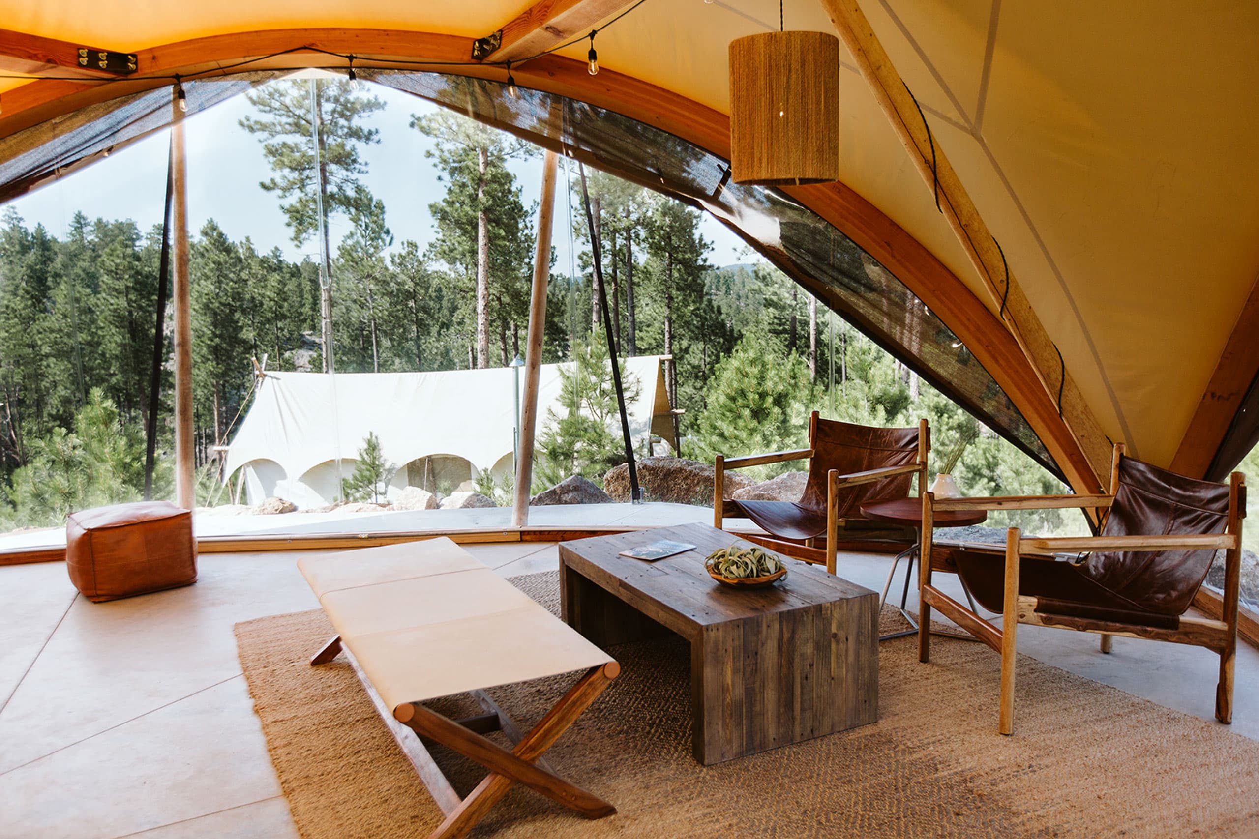 Interior view of a glamping tent at Under Canvas Mount Rushmore in Keystone, South Dakota. The tent features modern furnishings and an expansive view of the surrounding forest.
