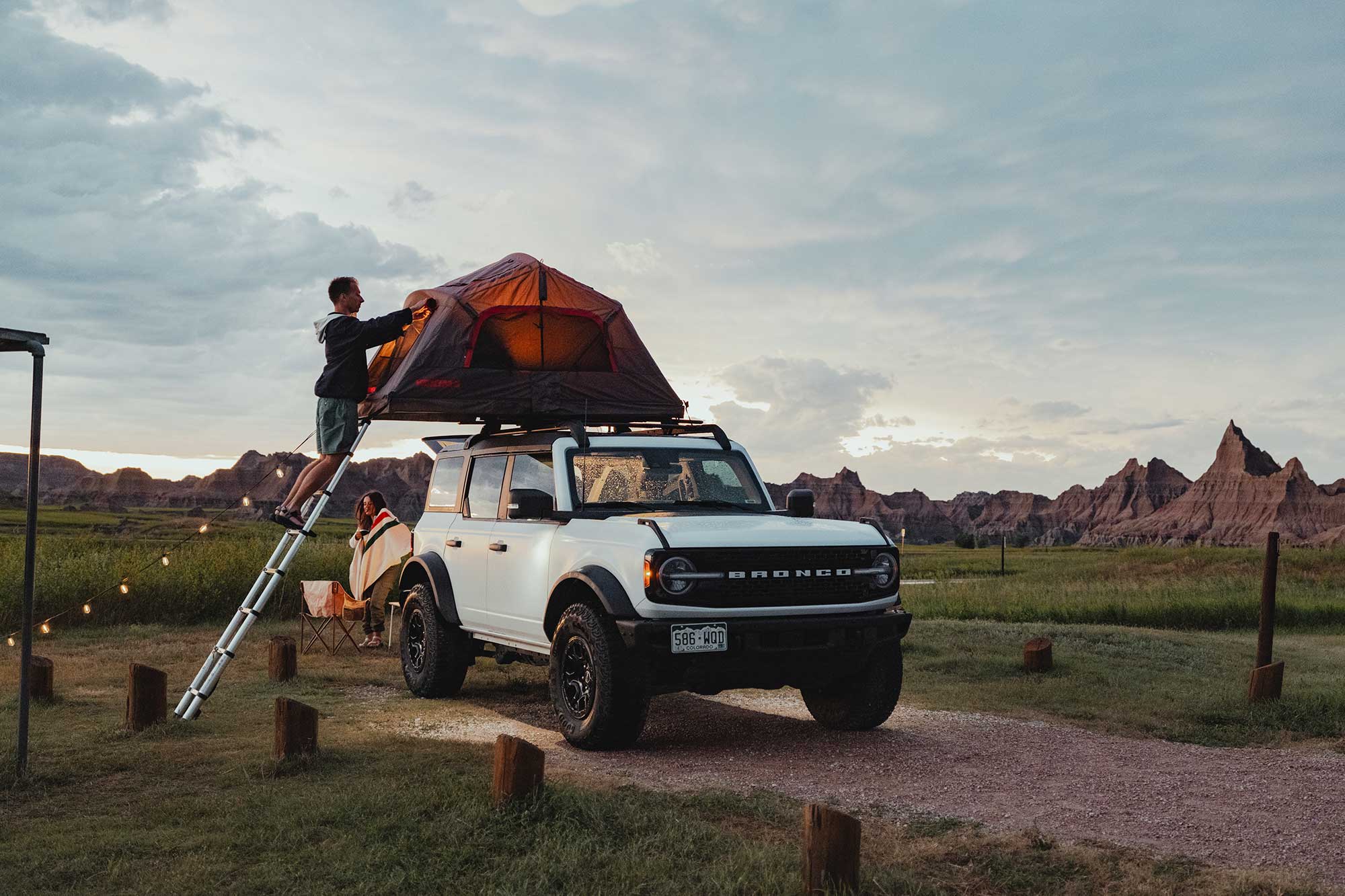 A man sets up a tent on top of an SUV at a scenic campground in Badlands National Park, South Dakota.