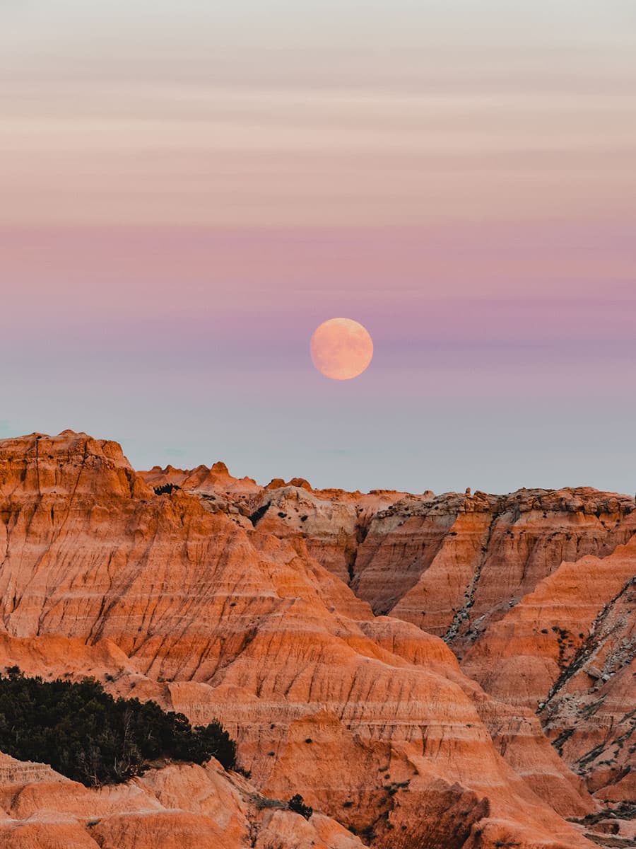 The Badlands of South Dakota are pictured at dusk with a full moon.