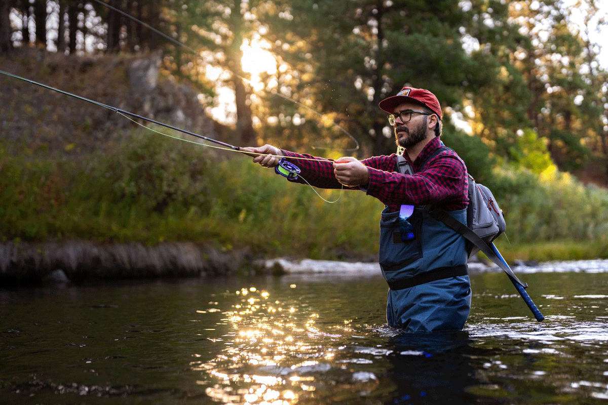 A man fly fishing wearing a red flannel with overalls, standing in high water level.