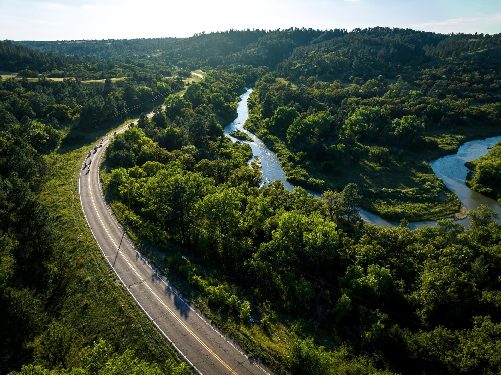 A road curves amongst thick green trees and flowing blue water