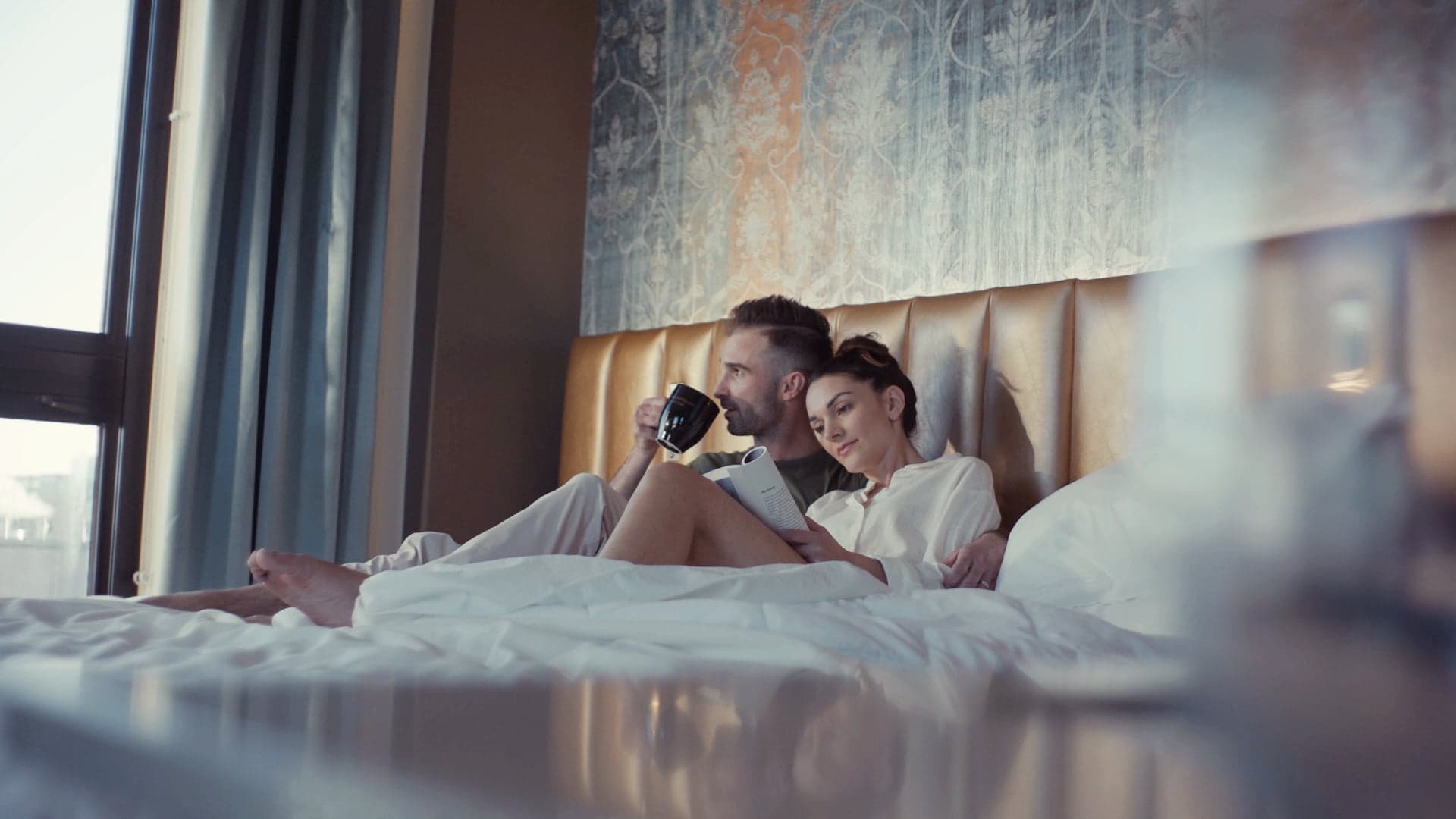 Husband drinking coffee and wife reading a book while enjoying a relaxing morning in their room at the Hotel on Phillips in Sioux Falls