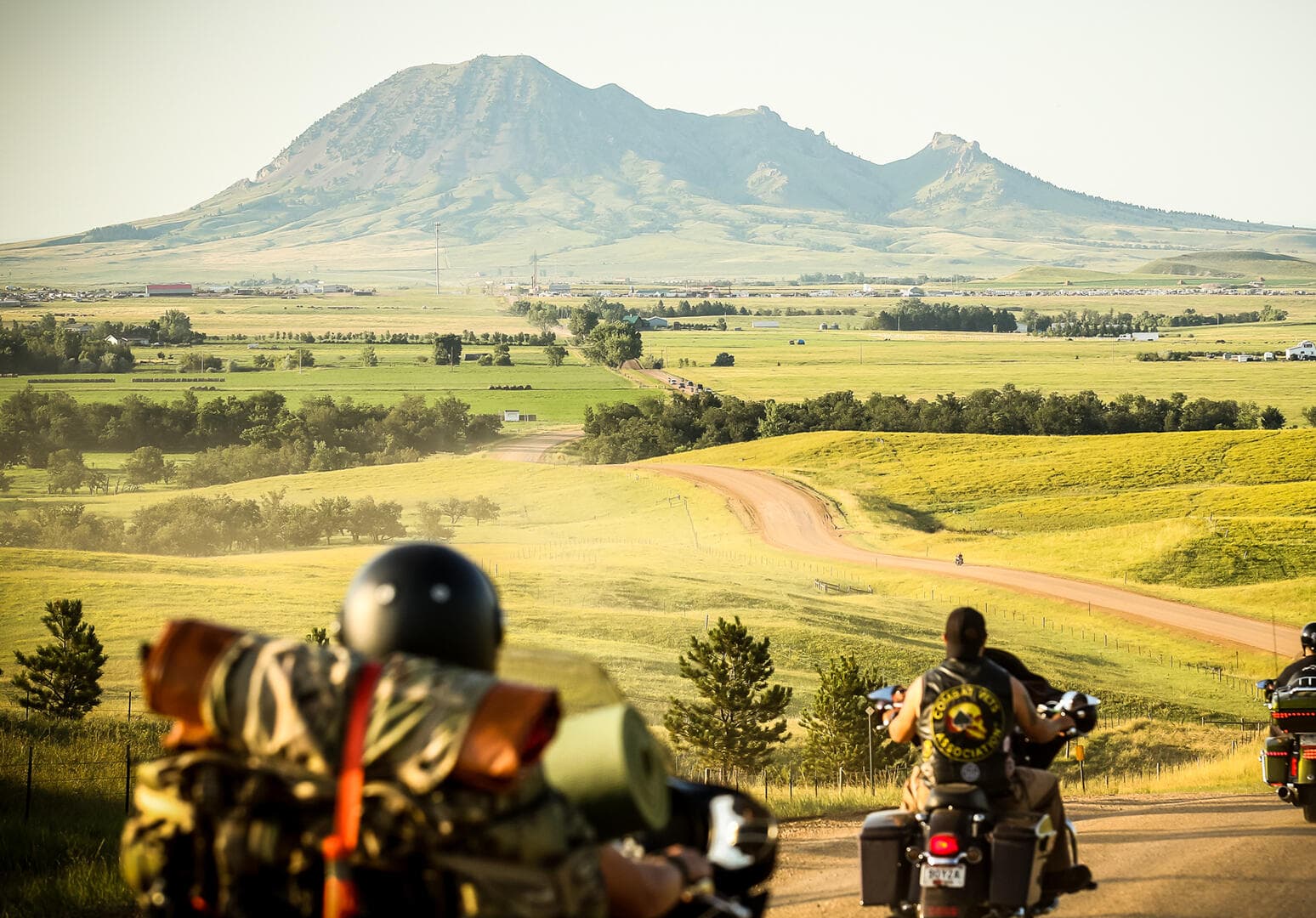 Motorcyclists facing out to a vast landscape with a mountain ahead of them