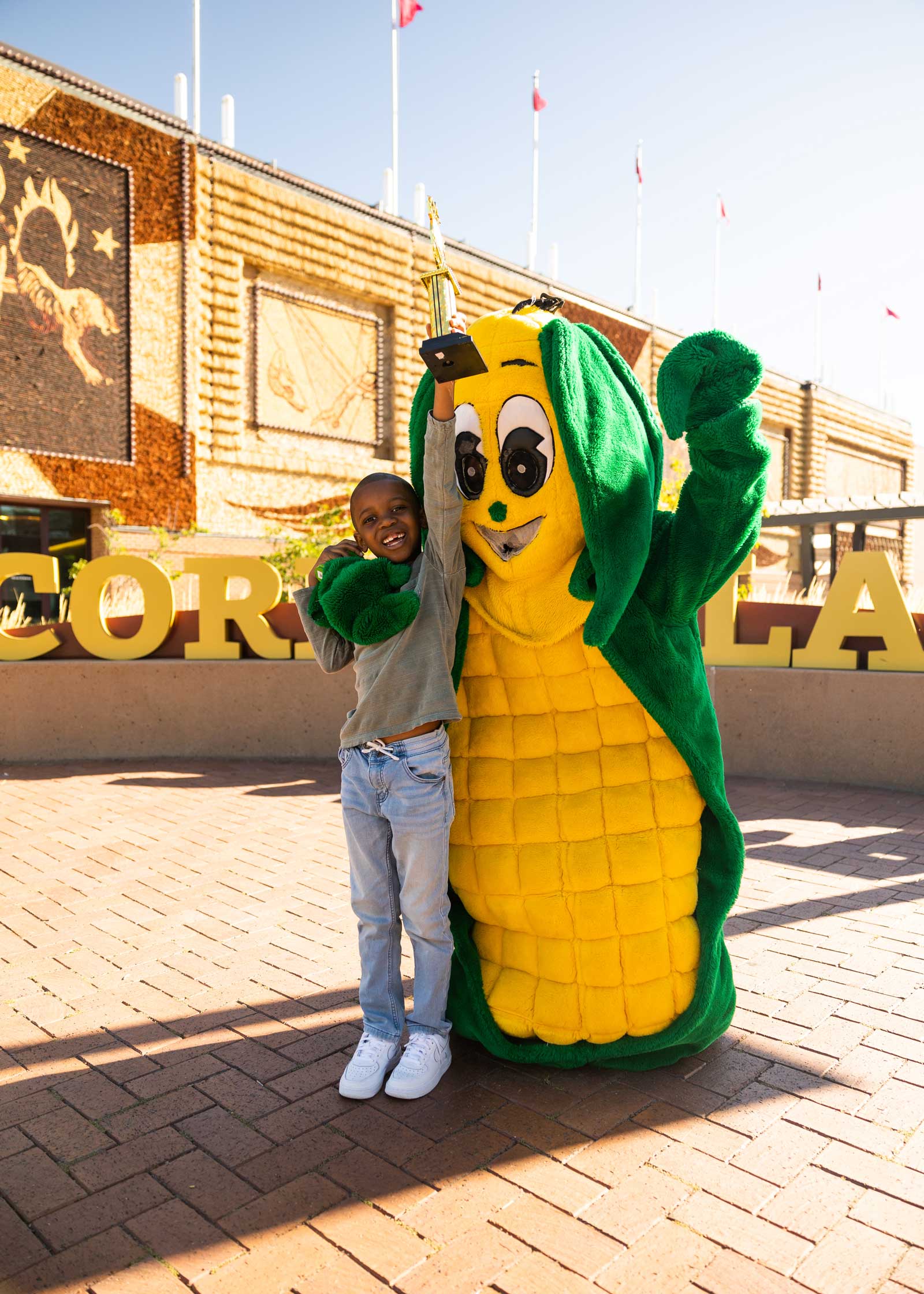 Tariq the "Corn Kid" posing with a Corn Mascot & trophy