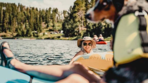Girl in a tube on a lake looking at the camera with an Aussie dog in the foreground on a kayak