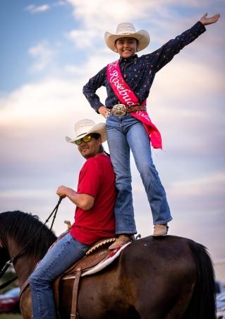 Young cowgirl standing on horse beside rider