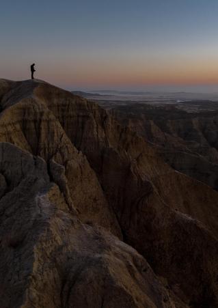 Wes Eisenhauer stands upon a Badlands bluff during a multi-colored sunrise at Badlands National Park