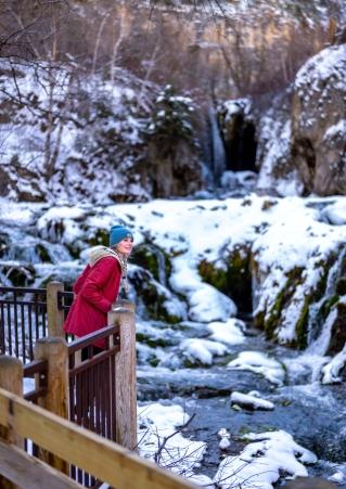 A woman gazes out over snow and water in Spearfish Canyon
