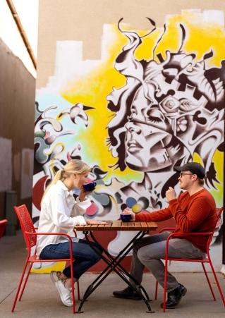 Two people enjoy a cup of coffee in front of a mural outside a coffee shop in Sioux Falls