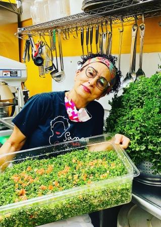 Sanaa holds a large bin of green food at her restaurant