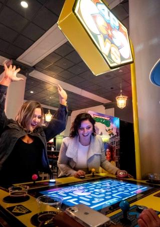 A woman celebrates as another looks on over a game of Pac-Man