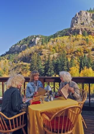 Three women enjoy an outdoor table with the Black Hills in the background