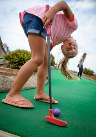 A child hangs her head upside-down over her ball on the mini golf course