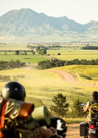 Motorcyclists facing out to a vast landscape with a mountain ahead of them