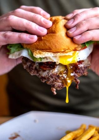 Close of man's hands holding the Fat Smitty Burger with egg yolk dripping off smashed beef patty at Black Hills Burger and Bun in Custer. 