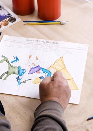 An Indigenous man makes colorful art on ledger paper