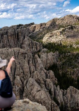 A female hiker points into the distance from atop a peak in Custer State Park. Custer, South Dakota.