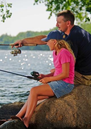 A father holds out a fishing ride beside his daughter as they fish together at Lake Kampeska