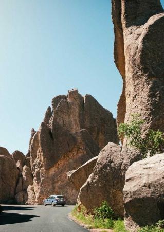 A car drives on a winding road surrounded by striking rock formations on the Needles Highway / Peter Norbeck National Scenic Byway in the Black Hills of South Dakota.