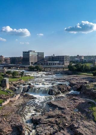 Falls Park in Sioux Falls, South Dakota, on a sunny day, with the city skyline in the background.