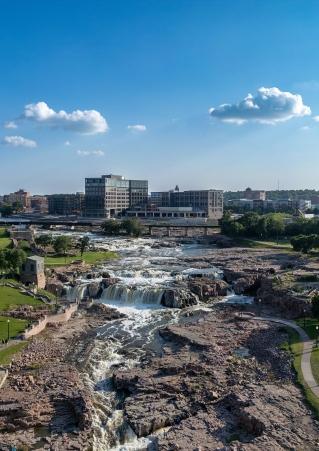 Falls Park in Sioux Falls, South Dakota, on a sunny day, with the city skyline in the background.