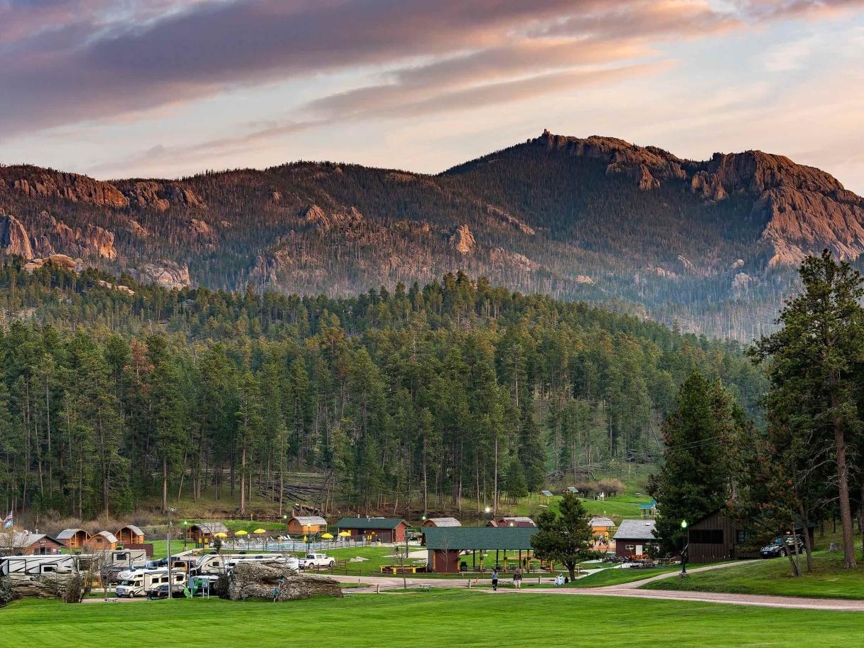 A campground filled with RVs spreads out beneath a dramatic mountain range in the Black Hills of South Dakota. Mount Rushmore KOA at Palmer Gulch, Hill City, SD.
