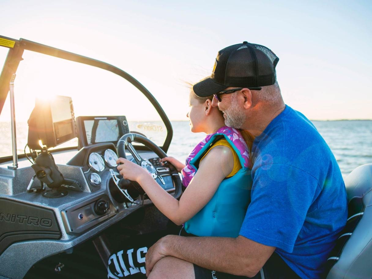 Dad and daughter driving a boat at sunset