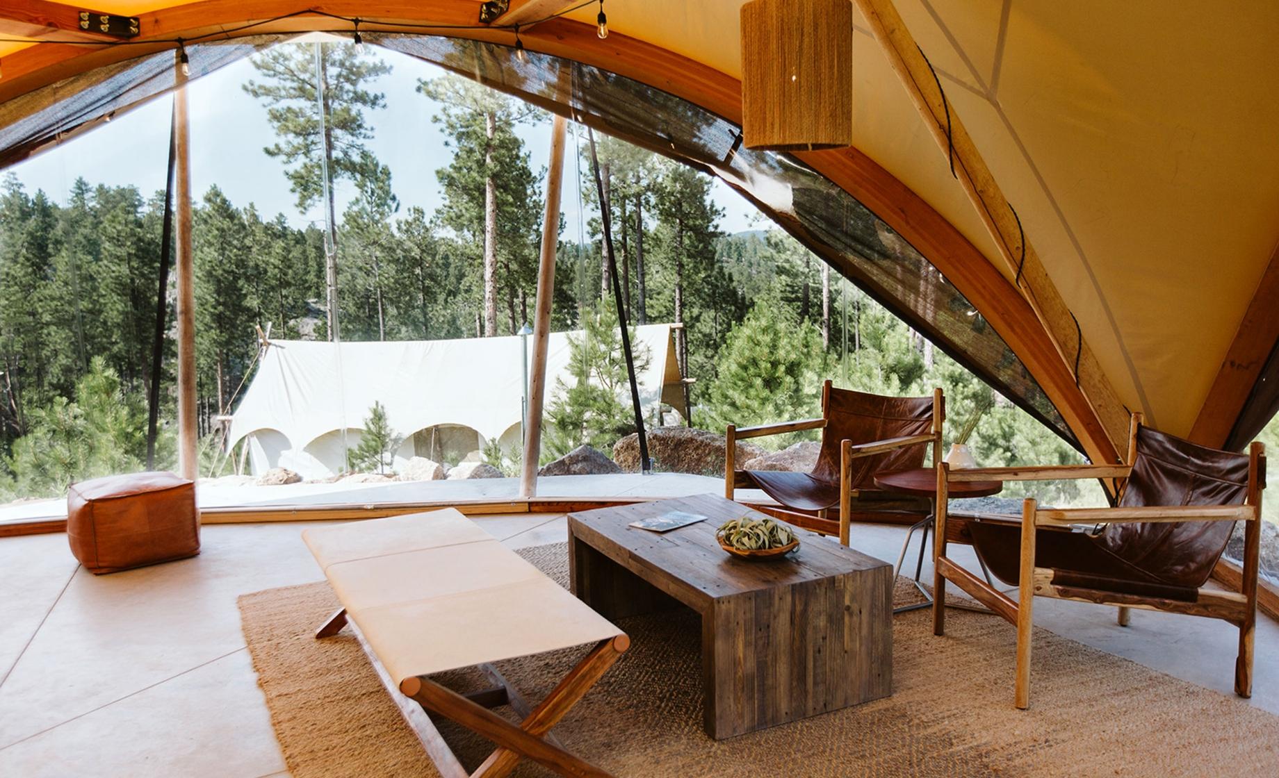 Interior view of a glamping tent at Under Canvas Mount Rushmore in Keystone, South Dakota. The tent features modern furnishings and an expansive view of the surrounding forest.
