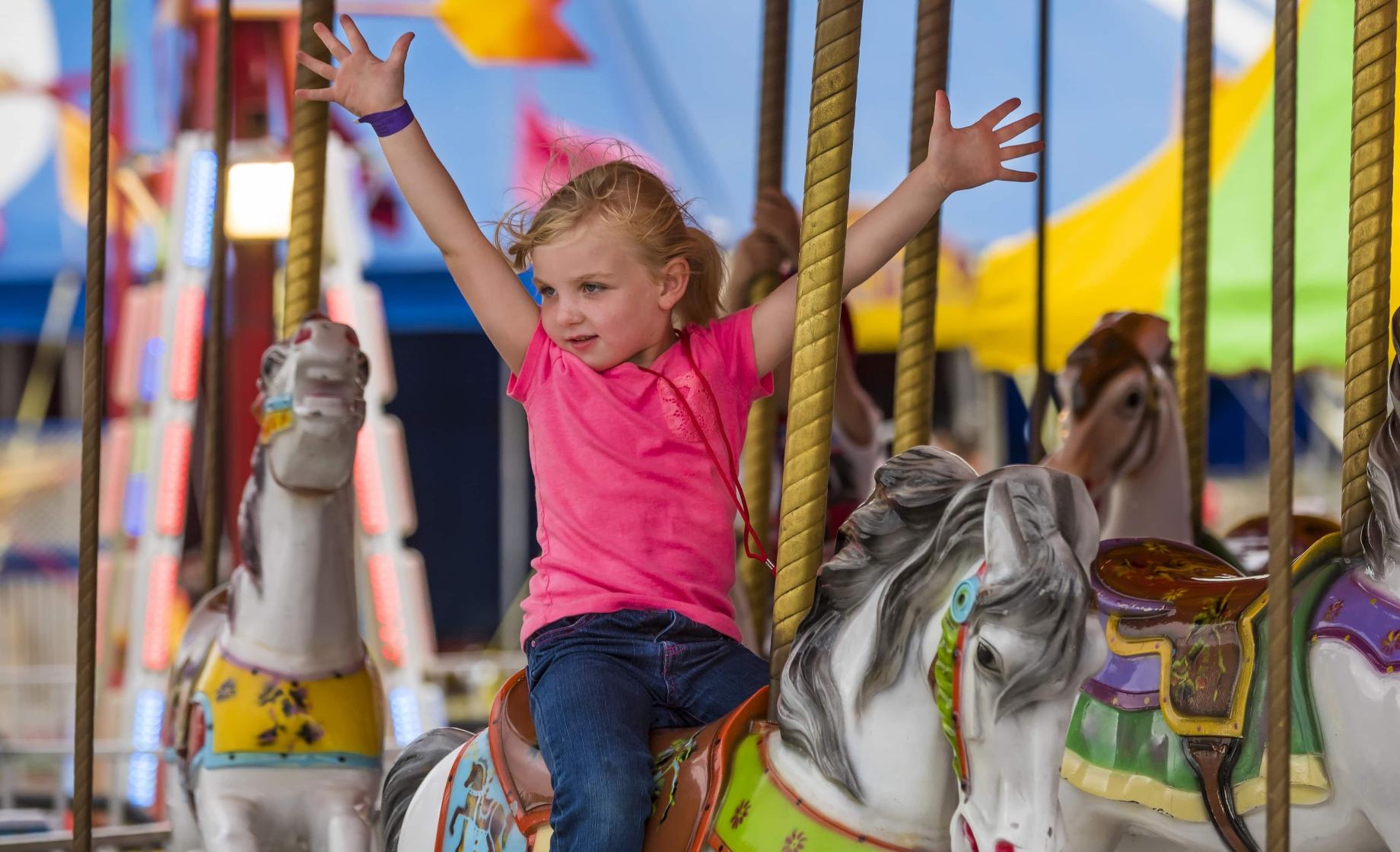 Girl riding a merry-go-round horse at the SD State Fair (wide shot)