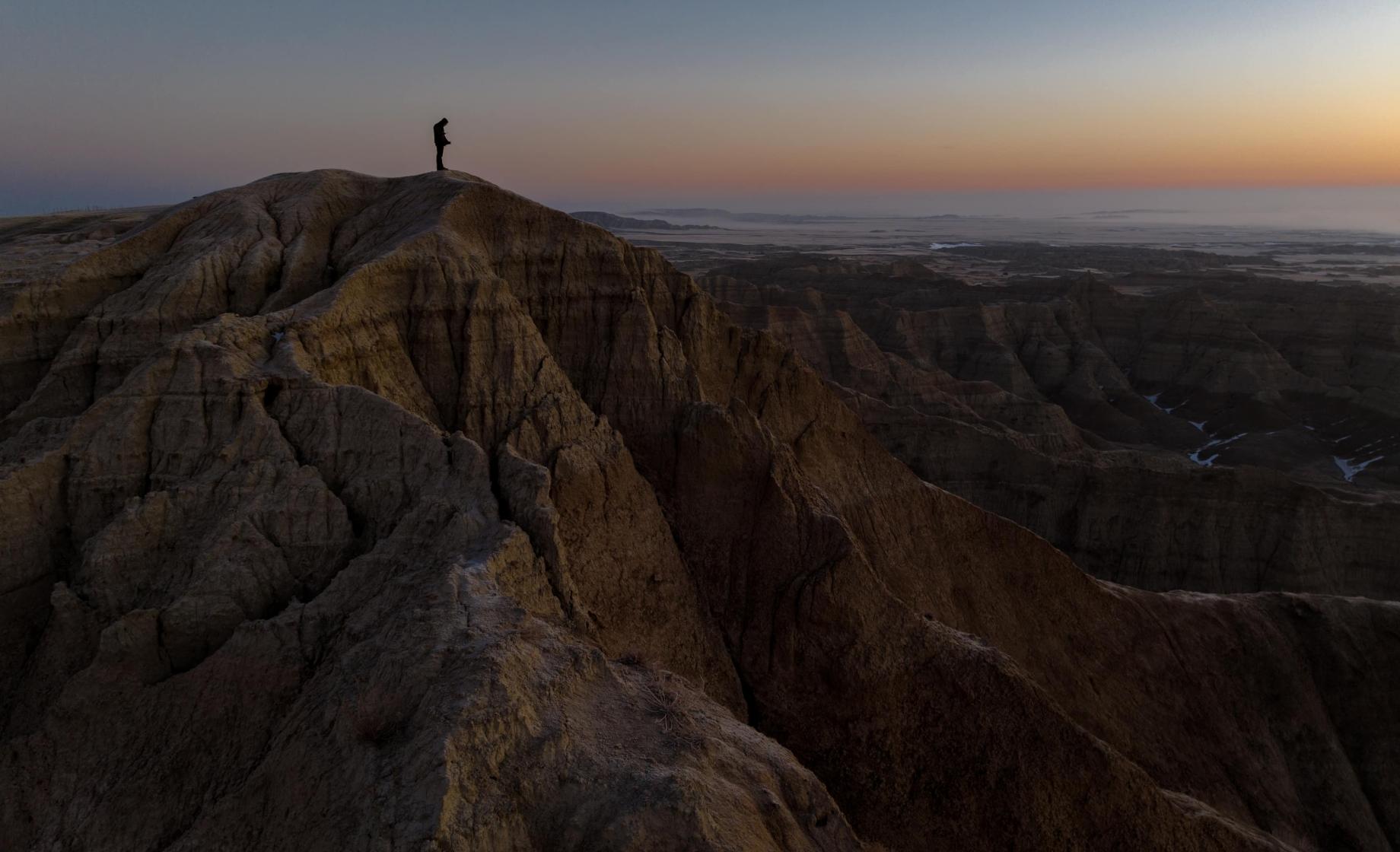 Wes Eisenhauer stands upon a Badlands bluff during a multi-colored sunrise at Badlands National Park