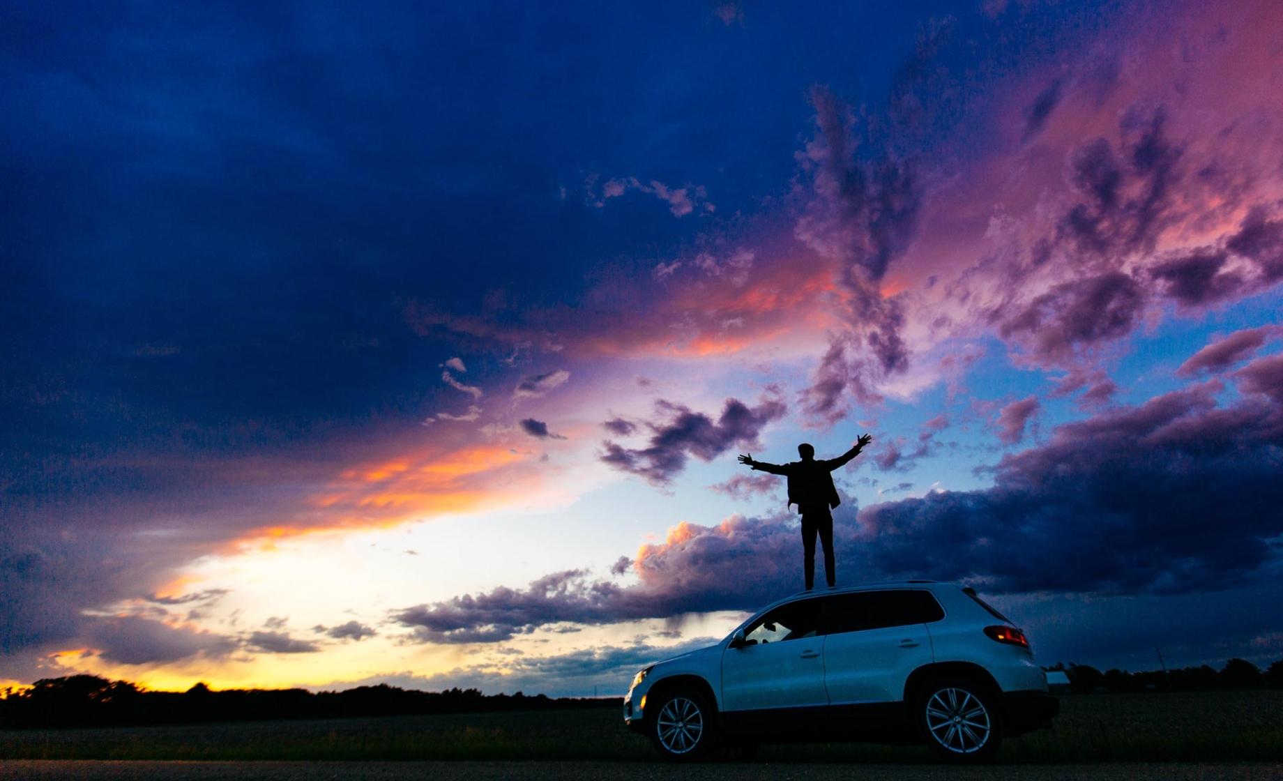 person standing on car roof at sunset