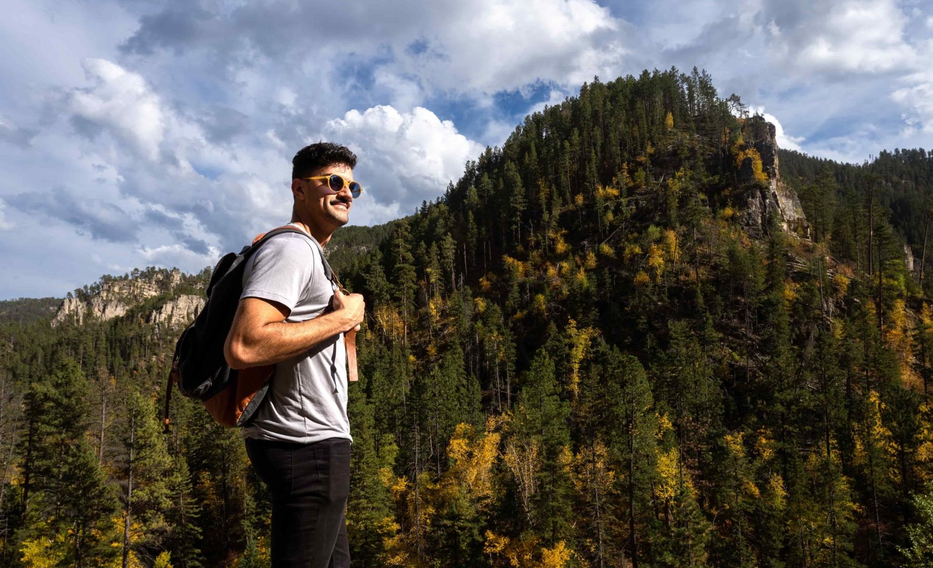 A man stands in sunglasses amongst the trees and elevation of the Black Hills National Forest
