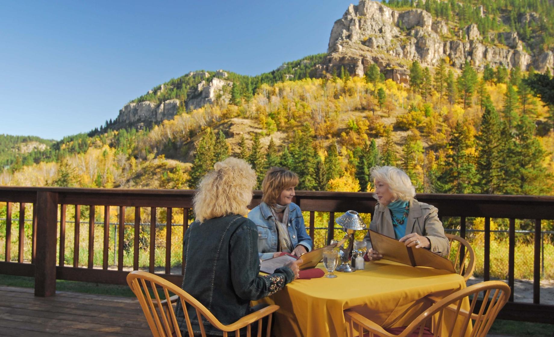 Three women enjoy an outdoor table with the Black Hills in the background
