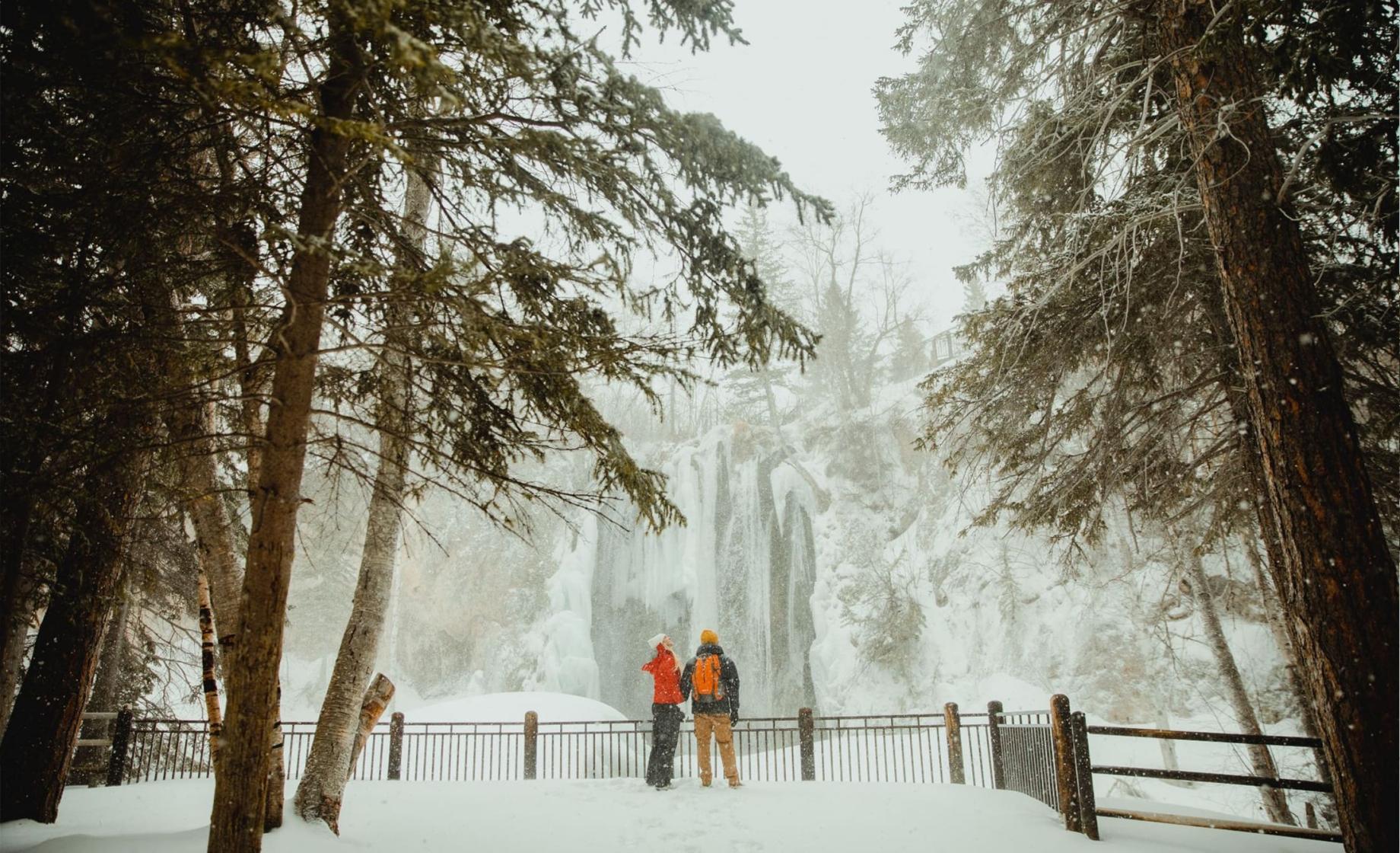 Two hikers in winter gear stand among the trees in a snowy Spearfish Canyon