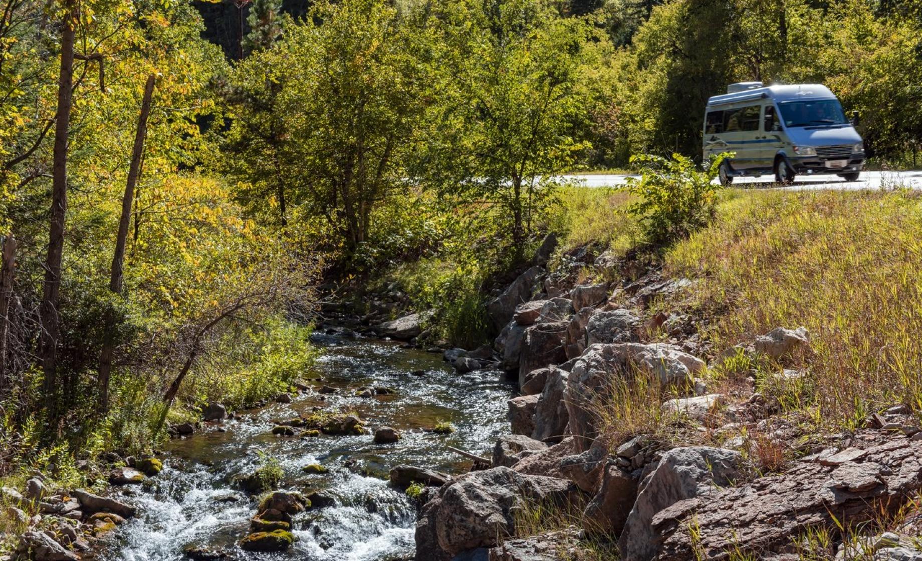 Silver van driving by a river through Spearfish Canyon in South Dakota.