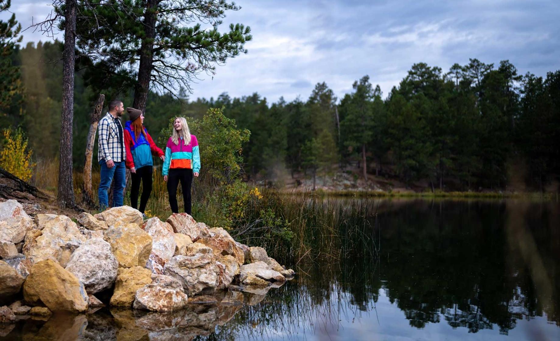 Three friends stand on the rocky shoreline of a lake at a resort in Custer State Park. Custer, South Dakota.