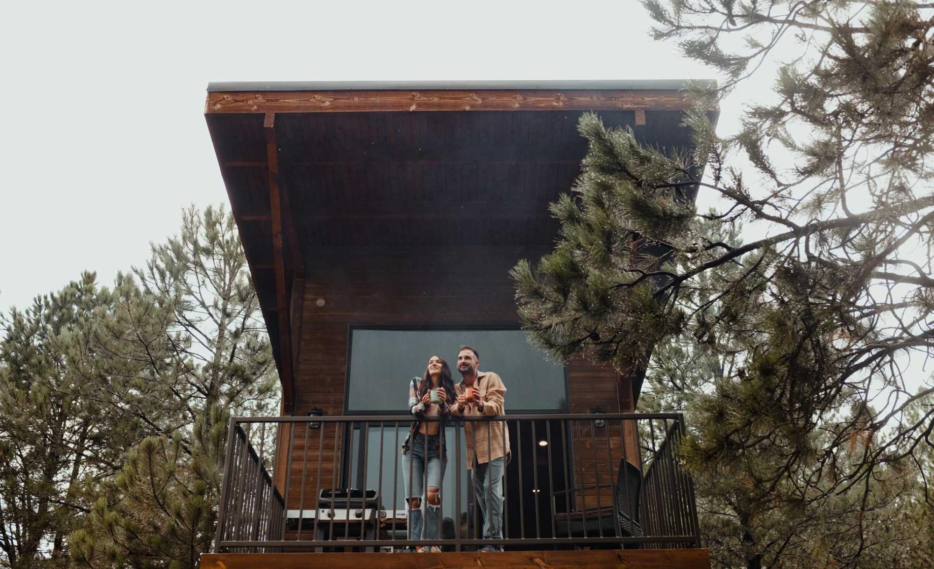 couple standing on a cabin balcony with coffee mugs