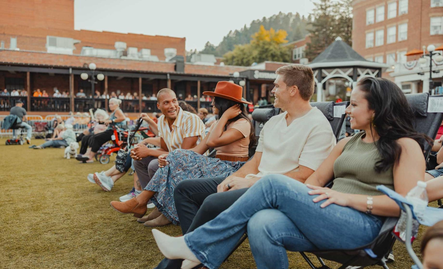 group of friends sitting in lawn chairs facing a stage out of frame