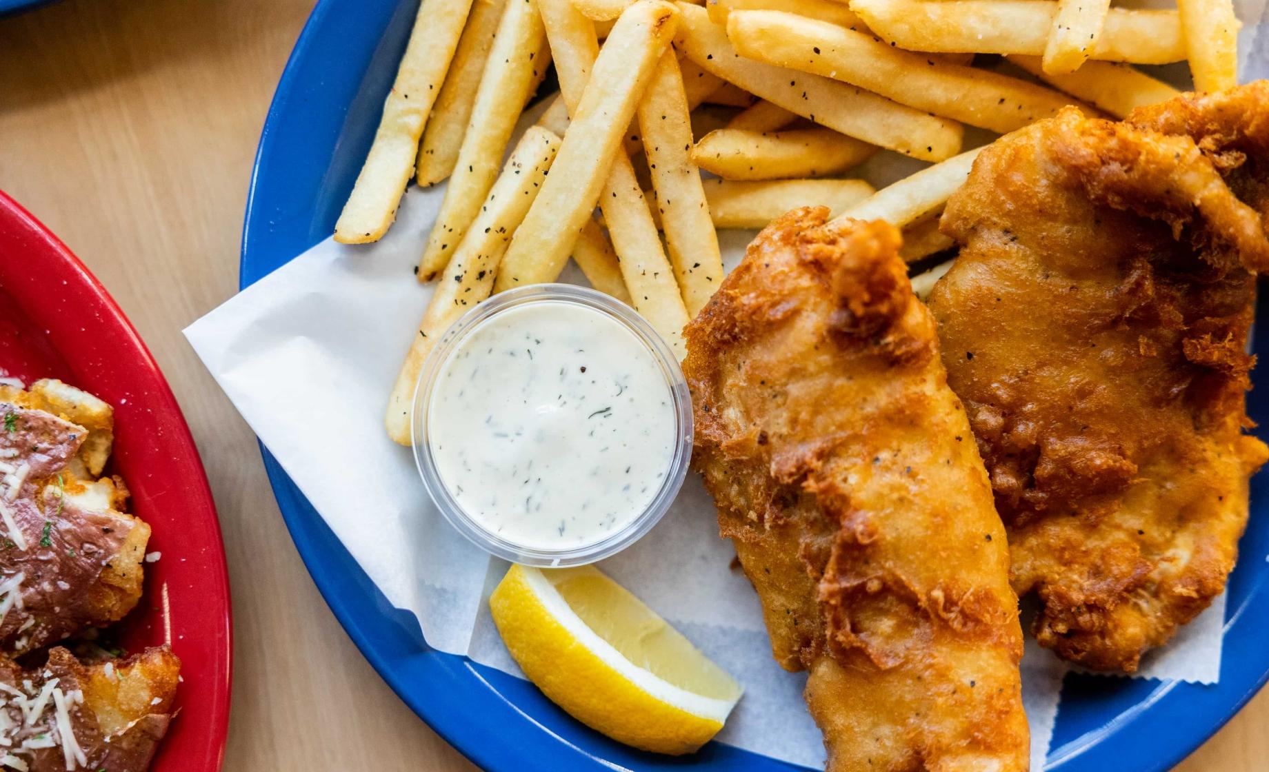 A blue plate with fried fish, French fries, tartar sauce and lemon