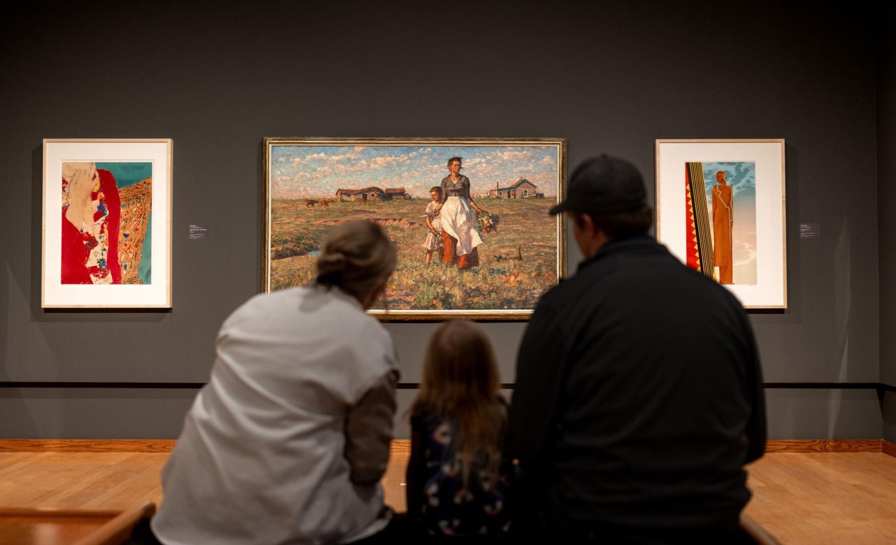 Two parents and a young child are pictured from behind as they admire a painting at the South Dakota Art Museum in Brookings, South Dakota.
