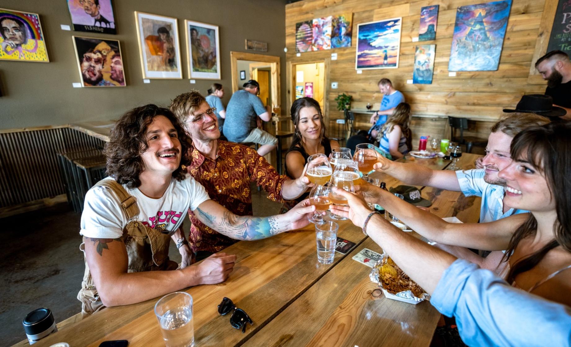 A group of people smile as they clink their beer glasses together over a wooden table at Lost Cabin Beer Co. in Rapid City