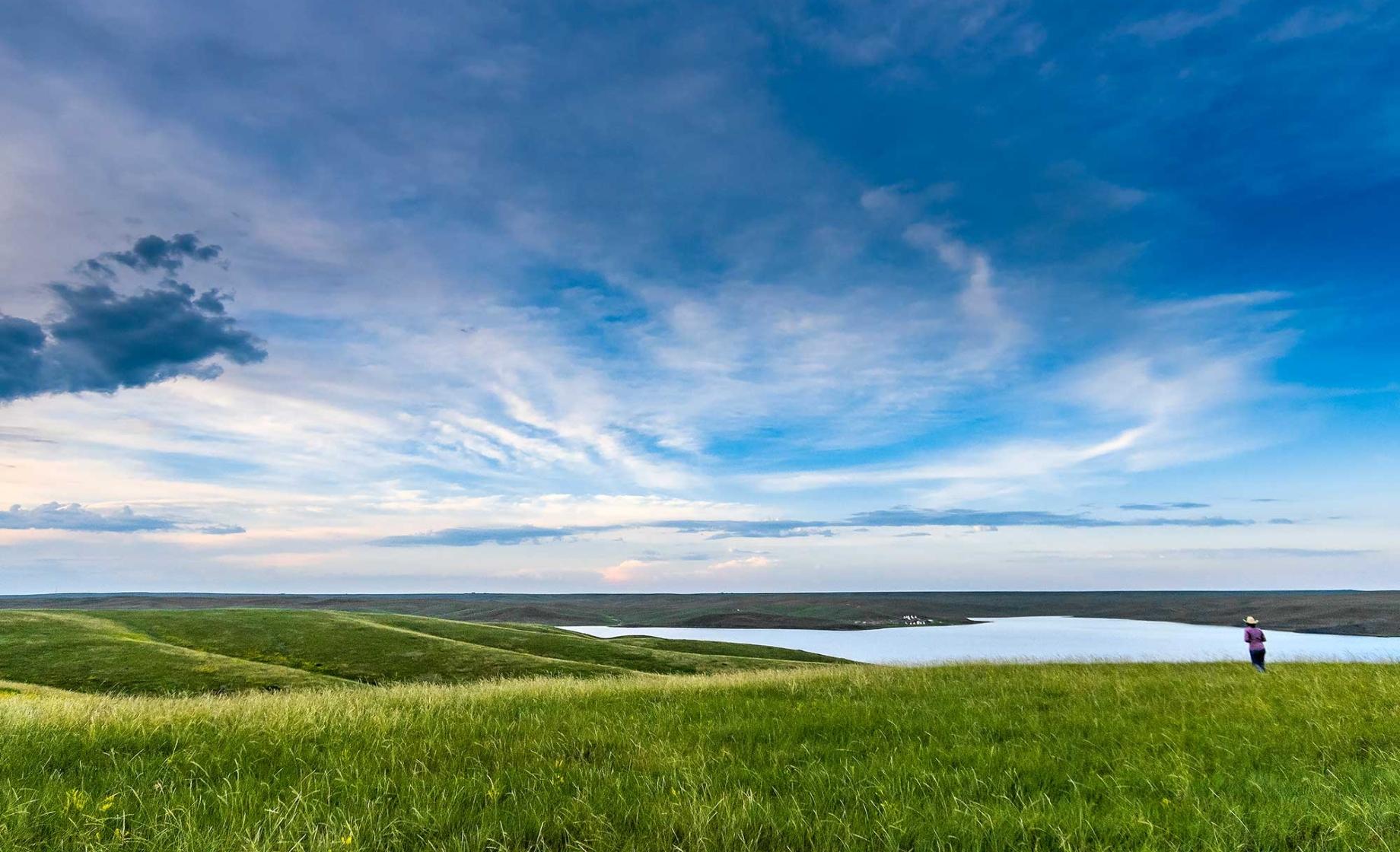 A person wearing a cowboy hat views an expansive prairie landscape under blue skies. Cheyenne River Reservation in South Dakota.