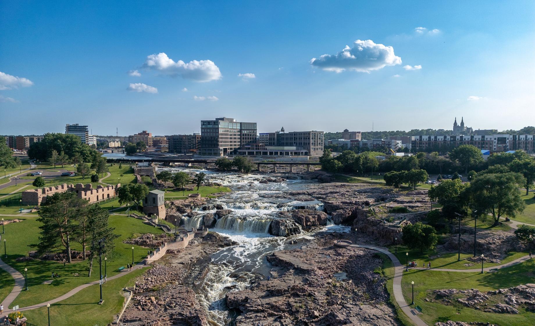 Falls Park in Sioux Falls, South Dakota, on a sunny day, with the city skyline in the background.