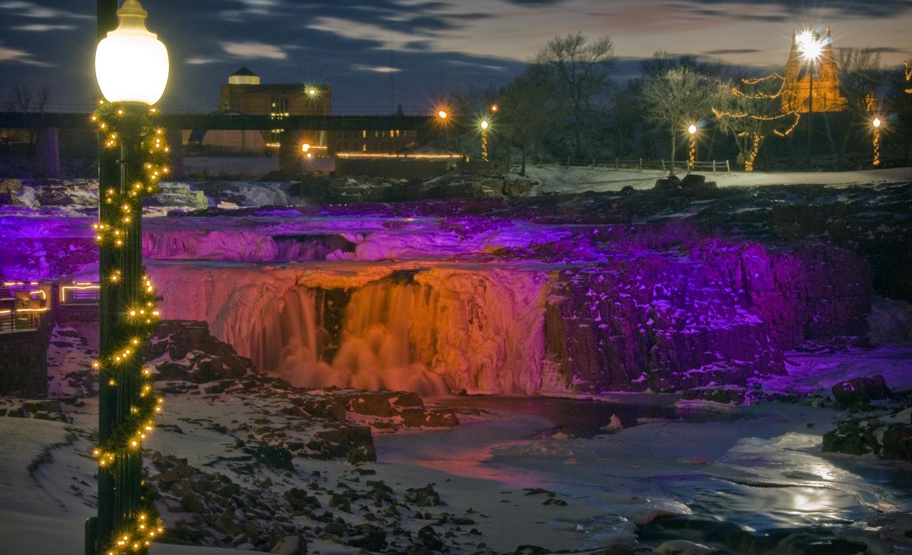 Purple and orange lights illuminate the waterfalls at Falls Park