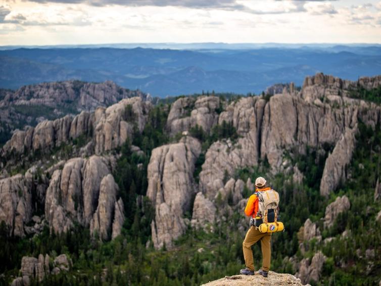 A man with a backpack stands overlooking the rock formations in Custer State Park