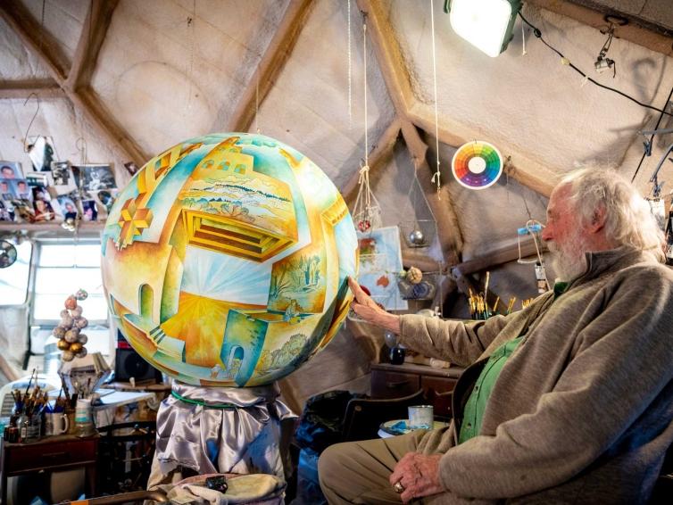 man reaching out to touch an artistic globe shaped piece of artwork hanging from the ceiling