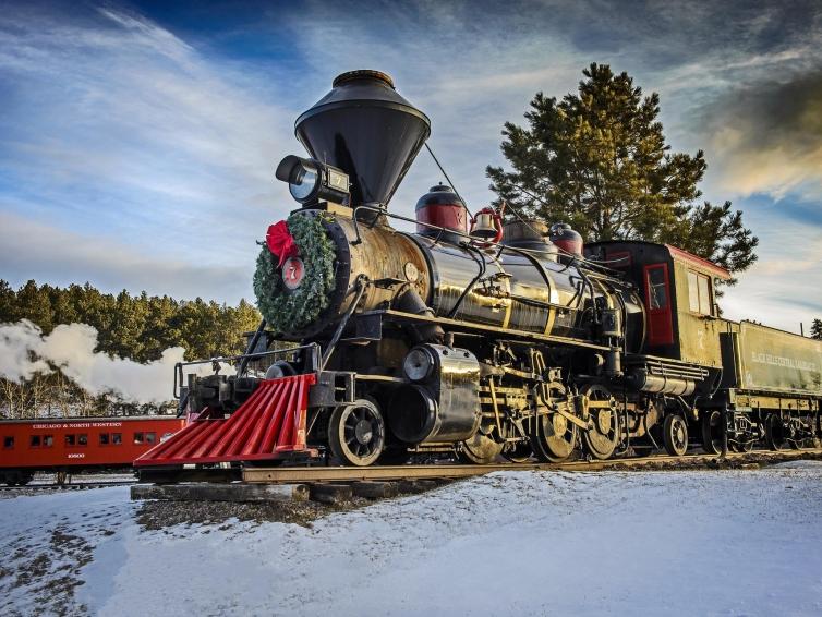 The 1880 Train during a snowy winter day, with a wreath on the front and smoke billowing around it.
