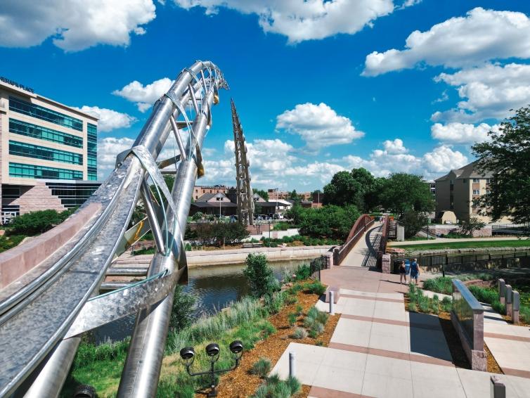 The Arc of Dreams in Sioux Falls reaches across the Big Sioux River on a sunny, slightly cloudy day.