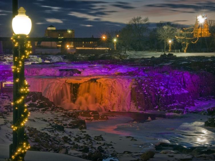 Purple and orange lights illuminate the waterfalls at Falls Park