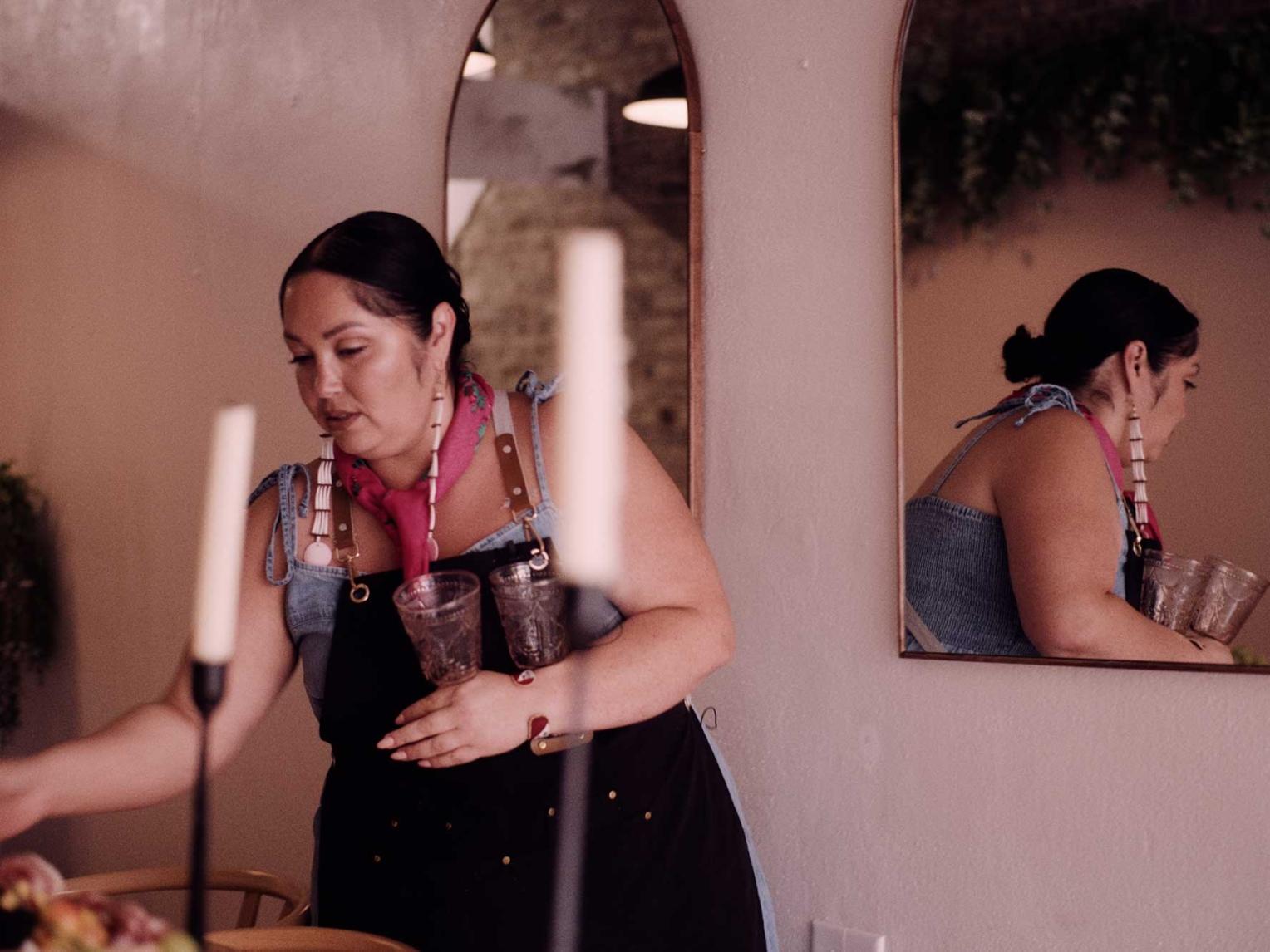 A woman, Chef Kimberly Tilsen-Brave Heart, sets a table, with two candles in the foreground.
